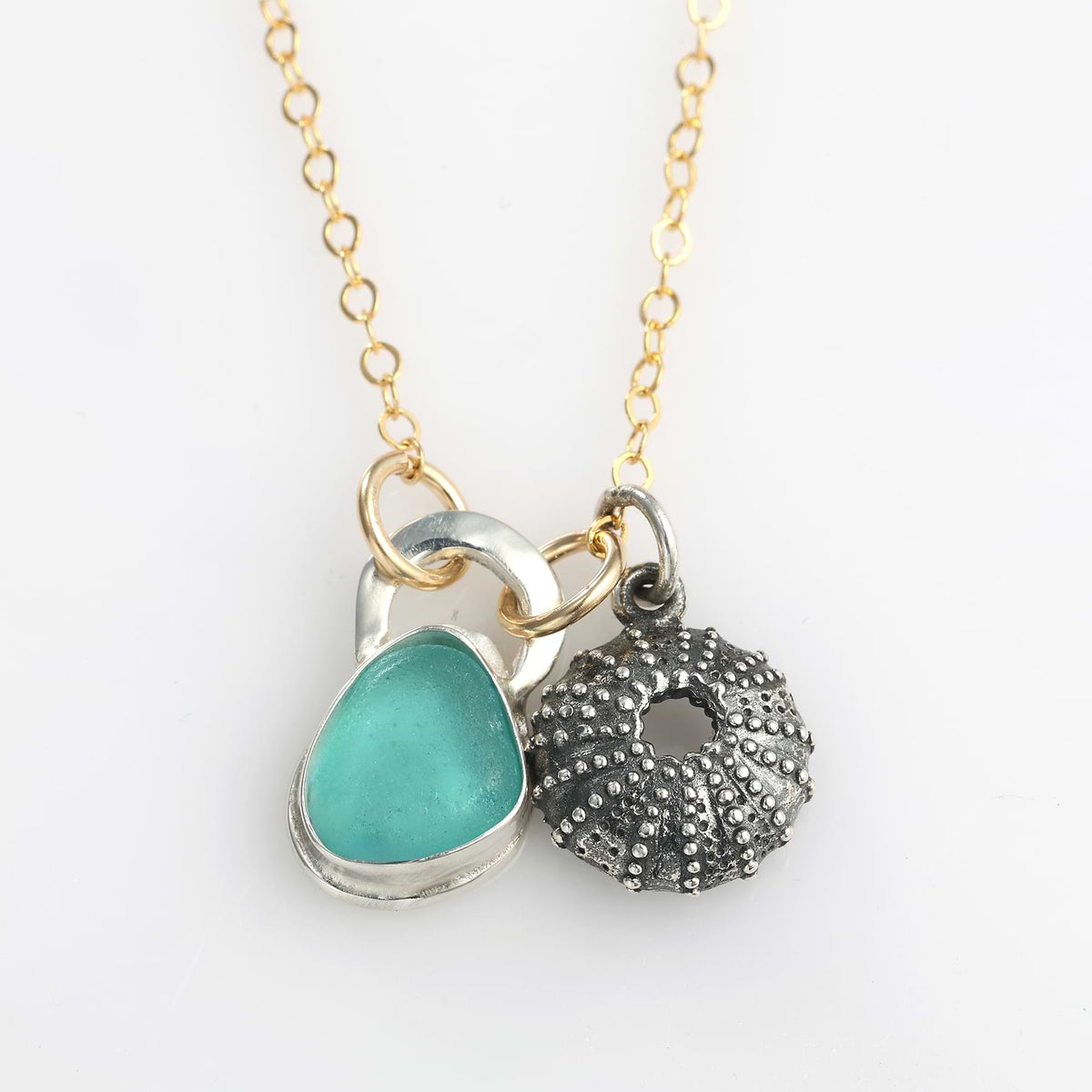 Close-up of the bezel-set aqua sea glass and detailed silver sea urchin charm on a gold-filled chain.