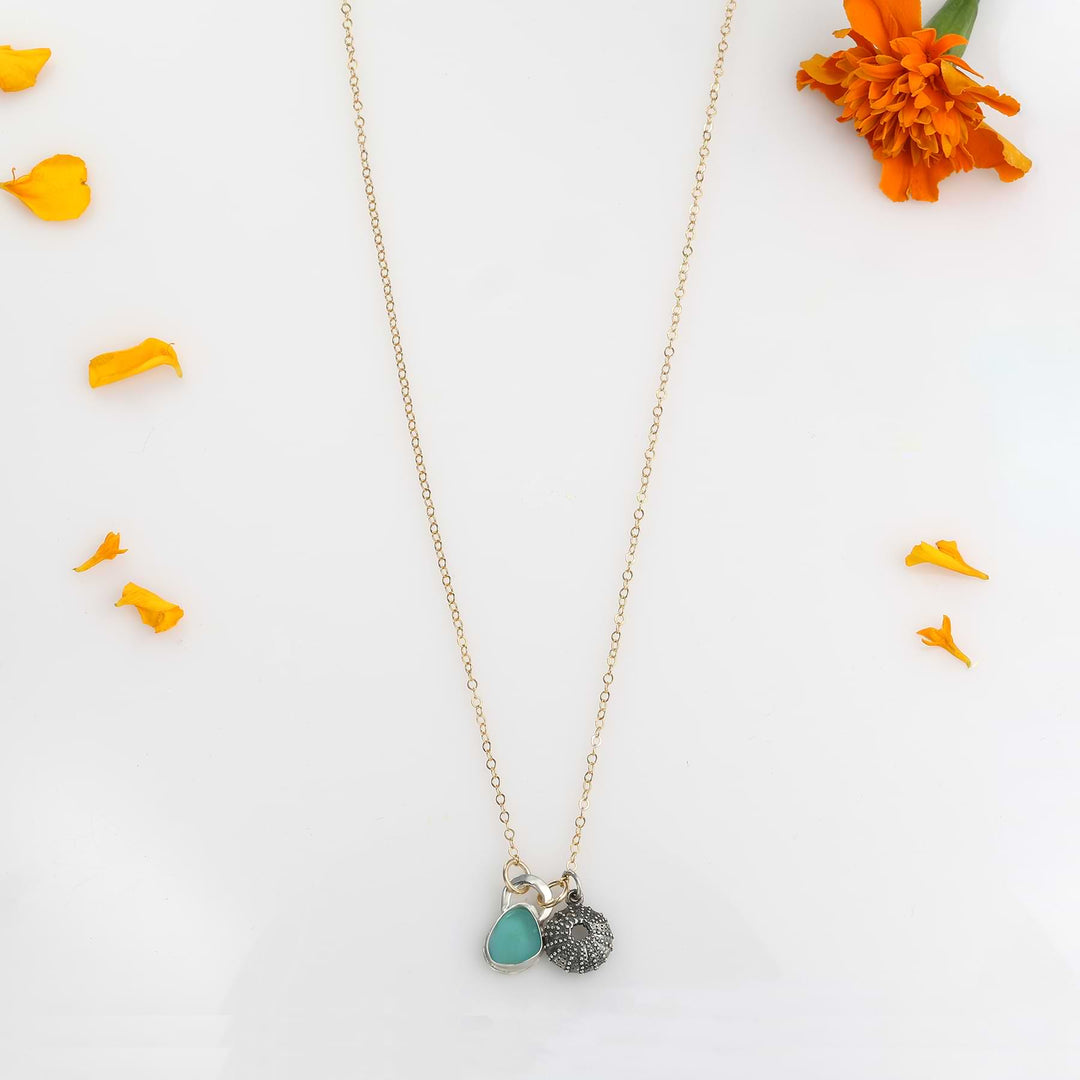 Top-down view of the 18-inch "Me and the Sea" necklace on a white surface with scattered orange petals.