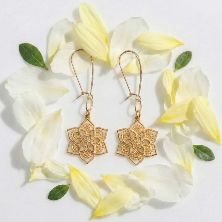 Golden mandala earrings arranged in a circle of soft yellow flower petals, highlighting the openwork design.