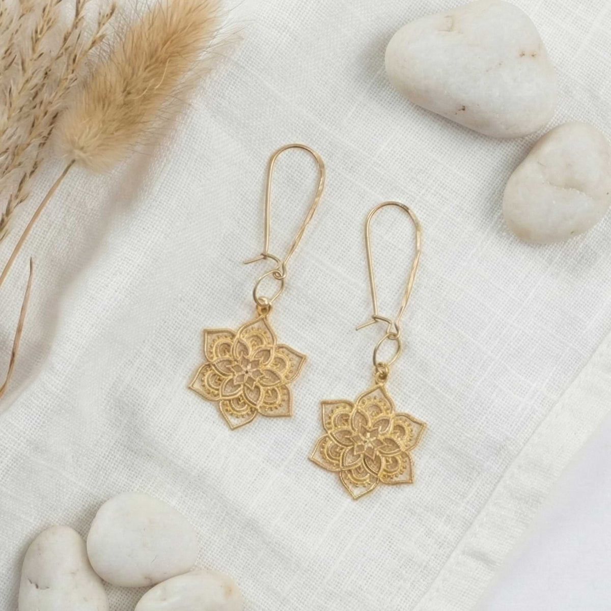 24k gold vermeil mandala earrings resting on white natural stones and linen fabric with dried pampas grass.