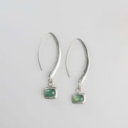 Minimalist silver drop earrings with long sculptural hooks featuring bezel-set green tourmaline cabochons.