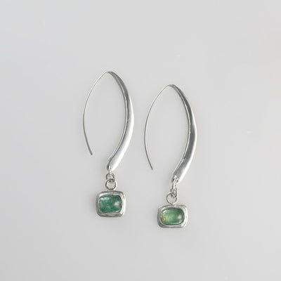 Minimalist silver drop earrings with long sculptural hooks featuring bezel-set green tourmaline cabochons.