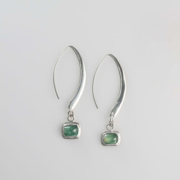 Minimalist silver drop earrings with long sculptural hooks featuring bezel-set green tourmaline cabochons.