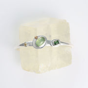 Top-down view of hammered sterling silver texture featuring fused 22k gold accents and a bezel-set green tourmaline.