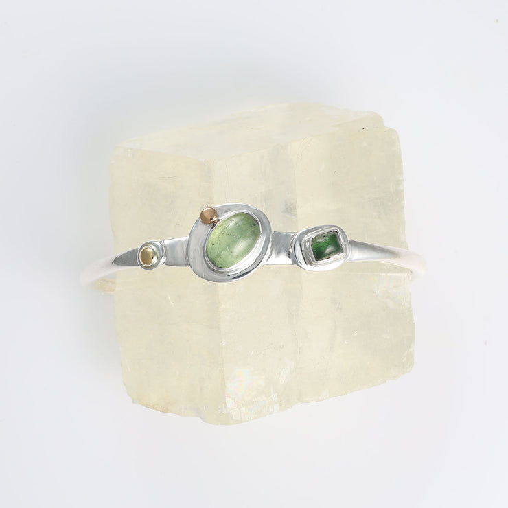 Top-down view of hammered sterling silver texture featuring fused 22k gold accents and a bezel-set green tourmaline.
