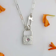 Close-up of hammered silver padlock pendant with pink sapphire, handcrafted on 18-inch paperclip chain.