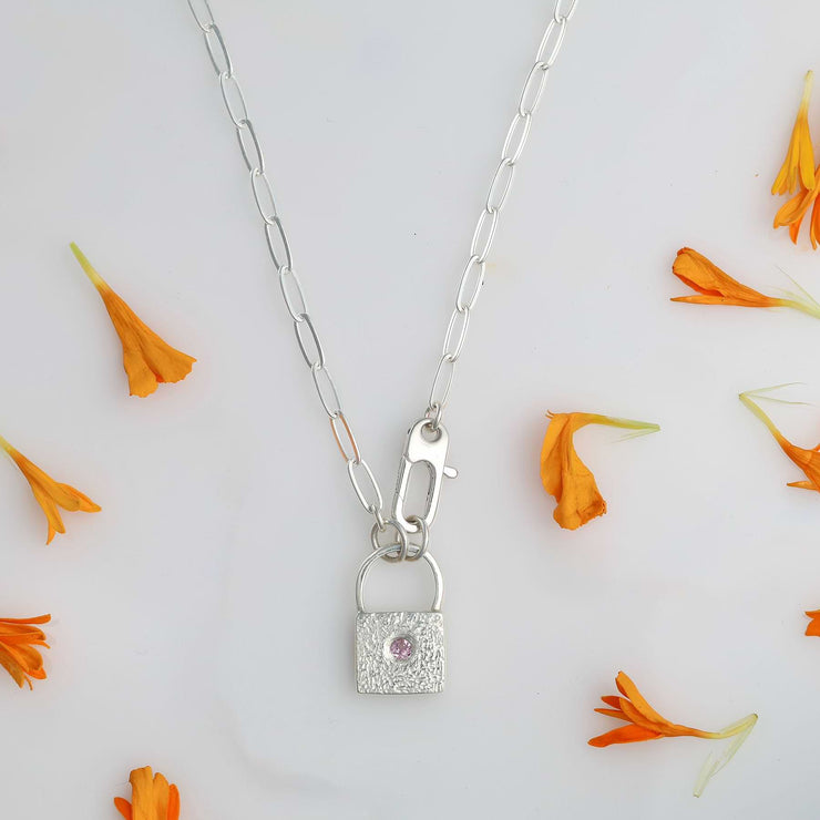 Tiny Argentium silver padlock pendant with flush-set pink sapphire on sterling silver paperclip chain, styled with orange flower petals.