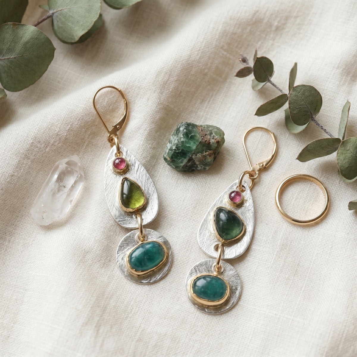 Pair of earrings with green gemstones on a textured surface with leaves.