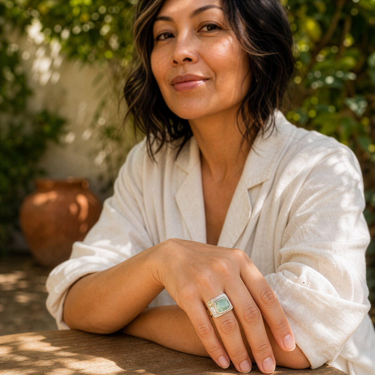 Woman wearing a white shirt with a green ring, sitting outdoors with greenery in the background