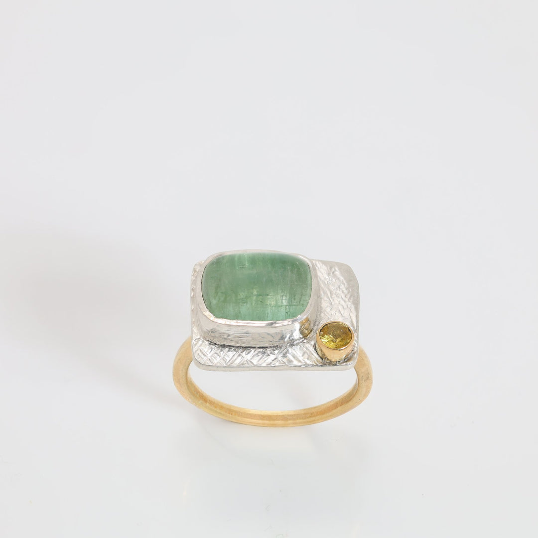 Silver ring with green gemstone and yellow gemstone on a white background