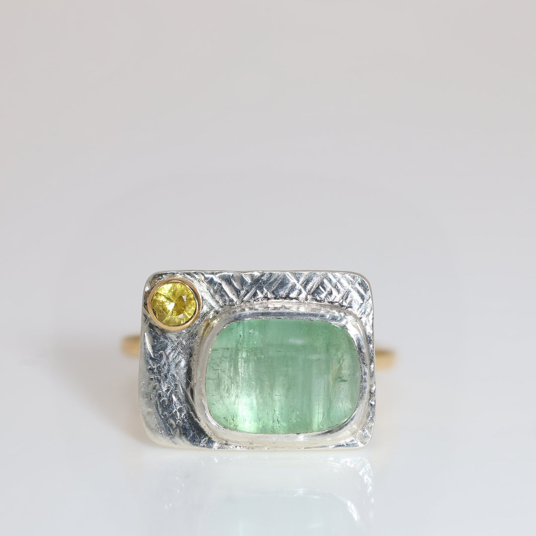 Silver ring with green and yellow gemstones on a white background