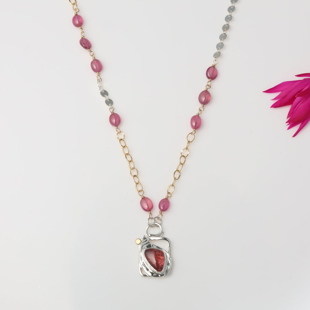 Necklace with pink beads and a silver pendant on a light gray background
