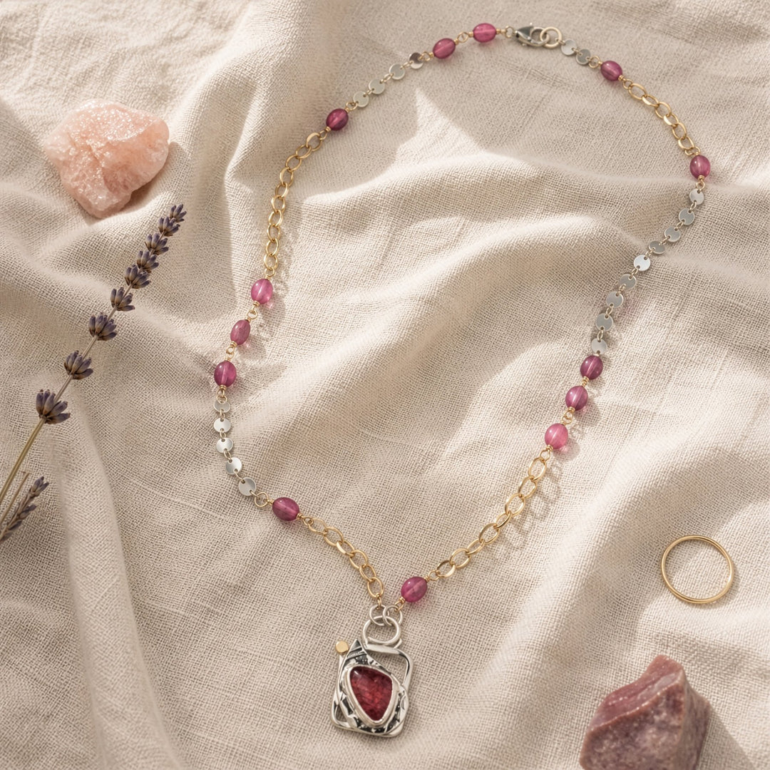 Necklace with pink beads and a red stone pendant on a beige fabric background