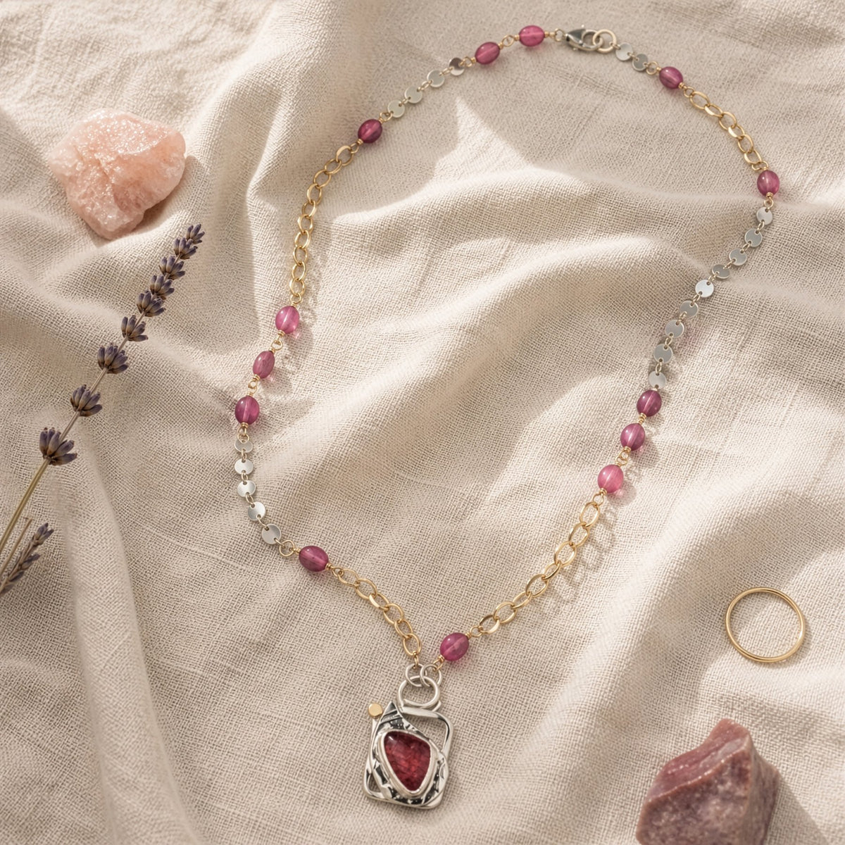 Necklace with pink beads and a red stone pendant on a beige fabric background