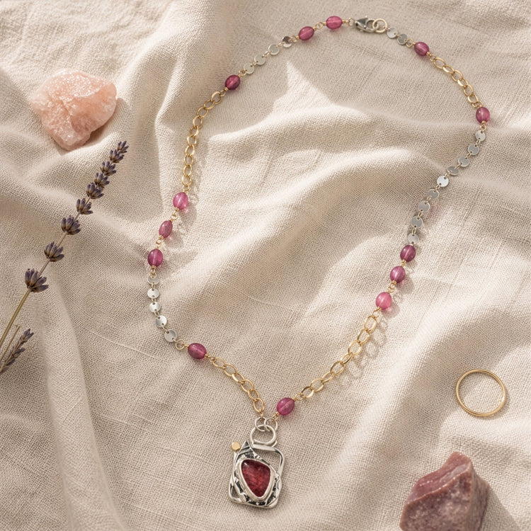 Necklace with pink beads and a red stone pendant on a beige fabric background