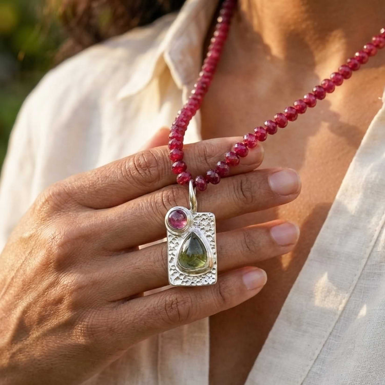 Woman wearing a short ruby beaded necklace with a silver tourmaline pendant, styled with a neutral linen top.