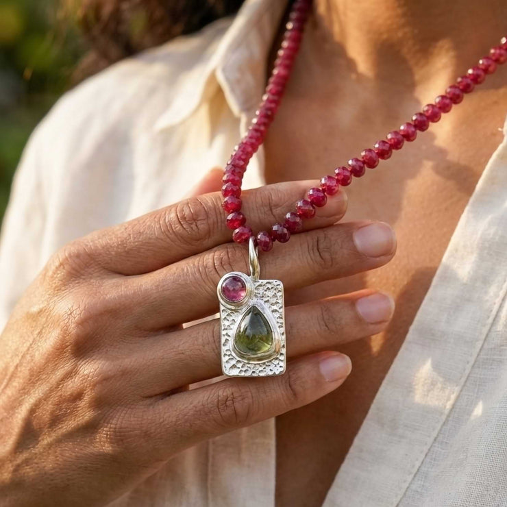 Woman wearing a short ruby beaded necklace with a silver tourmaline pendant, styled with a neutral linen top.