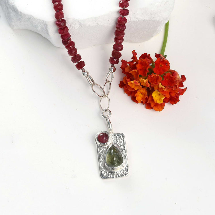 Macro detail of fine silver bezel settings holding tourmaline gems on a textured Argentium silver pendant, showing red silk knotting.