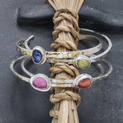 Four handcrafted Argentium silver cuff bracelets with fused gold and rose-cut sapphires in blue, pink, yellow, and orange.