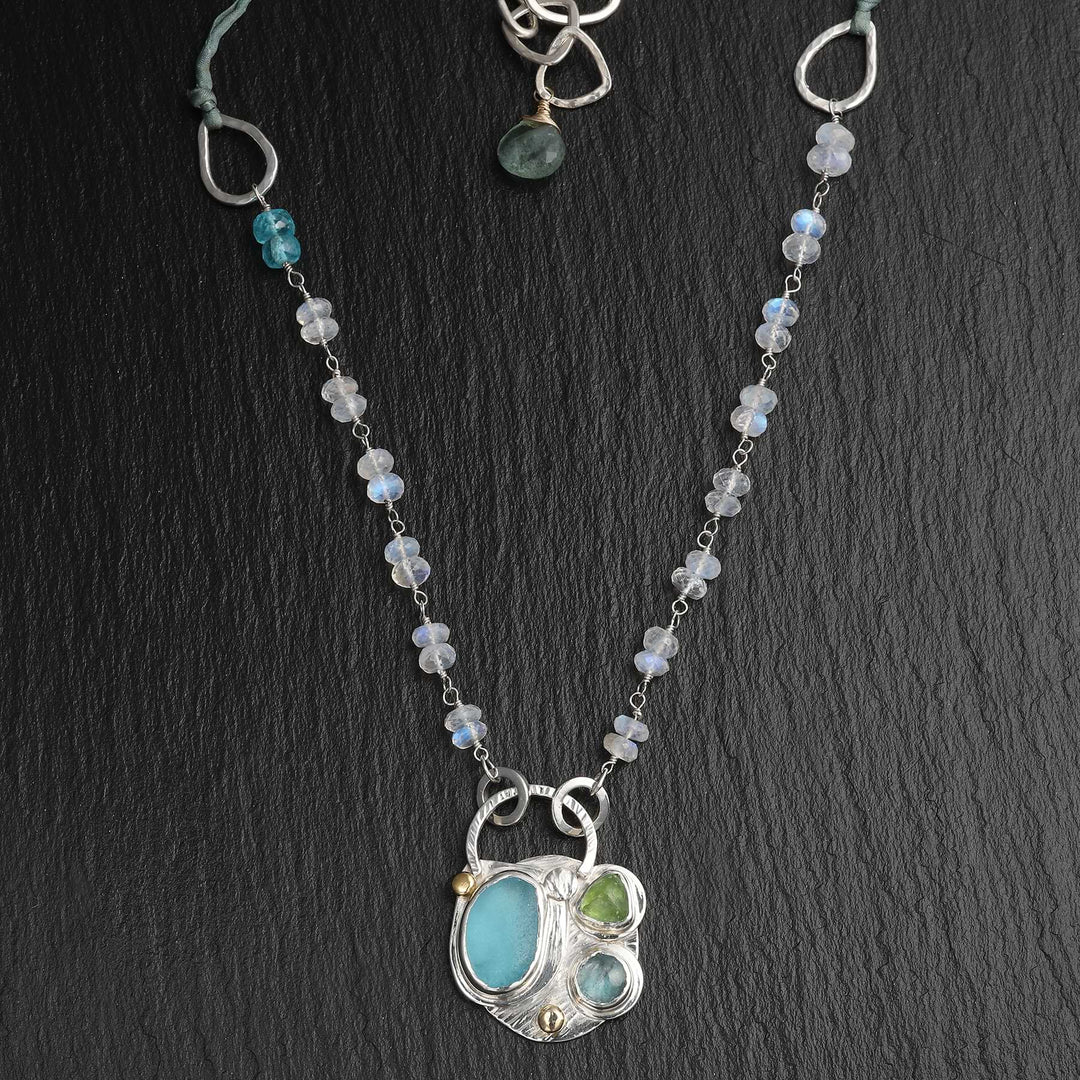 Textured silver pendant necklace featuring blue sea glass, kyanite, and green tourmaline, strung on a faceted moonstone chain.